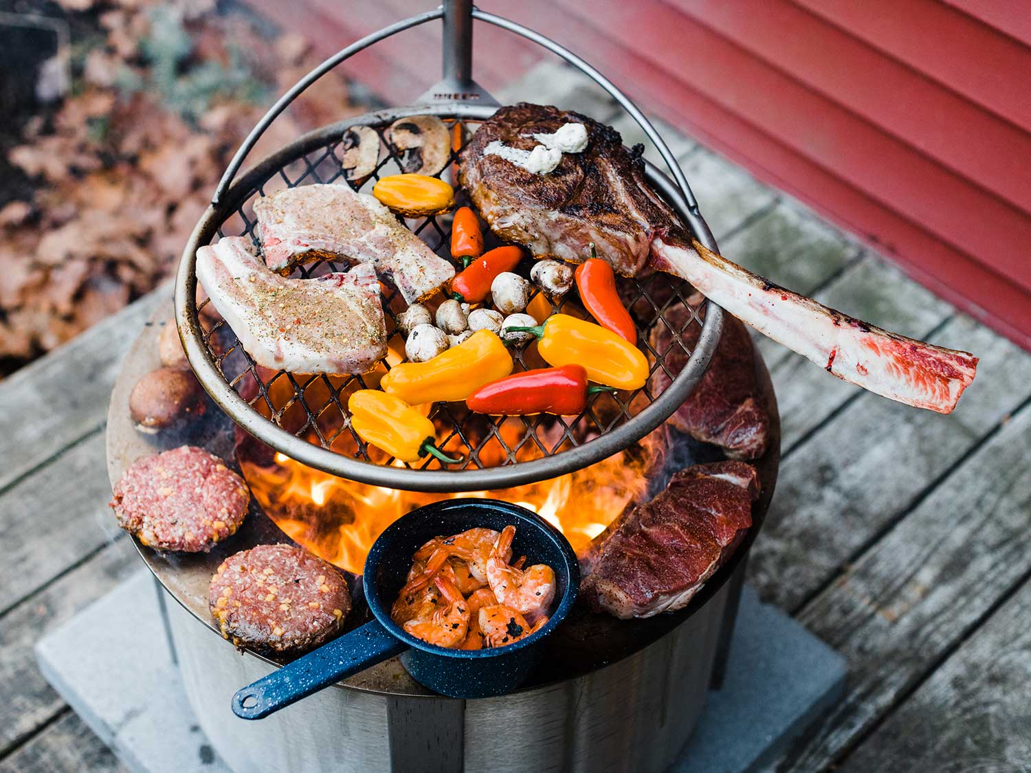 A Breeo X Series 24 smokeless fire pit being used to cook multiple steaks and other food items.