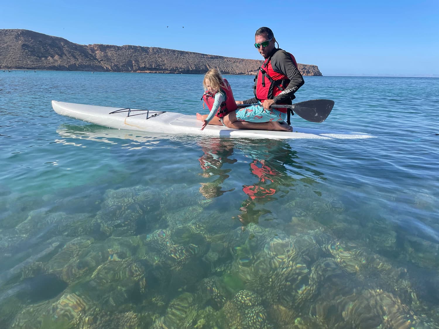 A father and daughter on a paddleboard in the water.