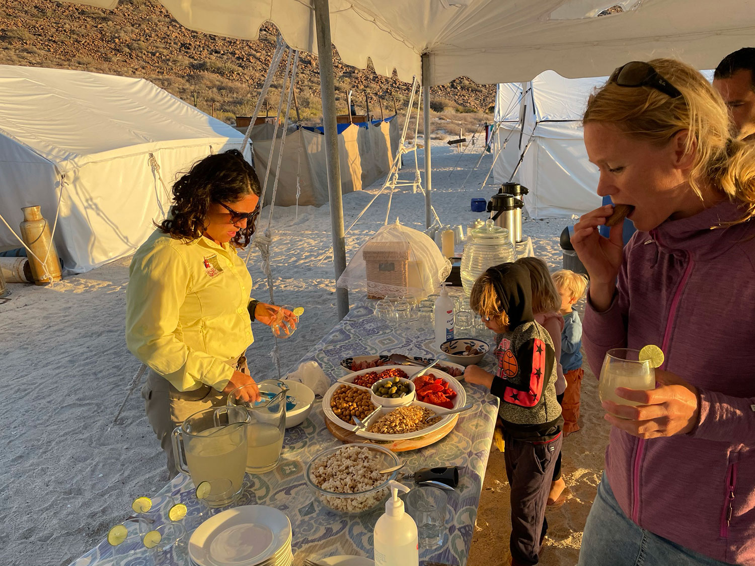 A family stands by a food table while camping on a beach.