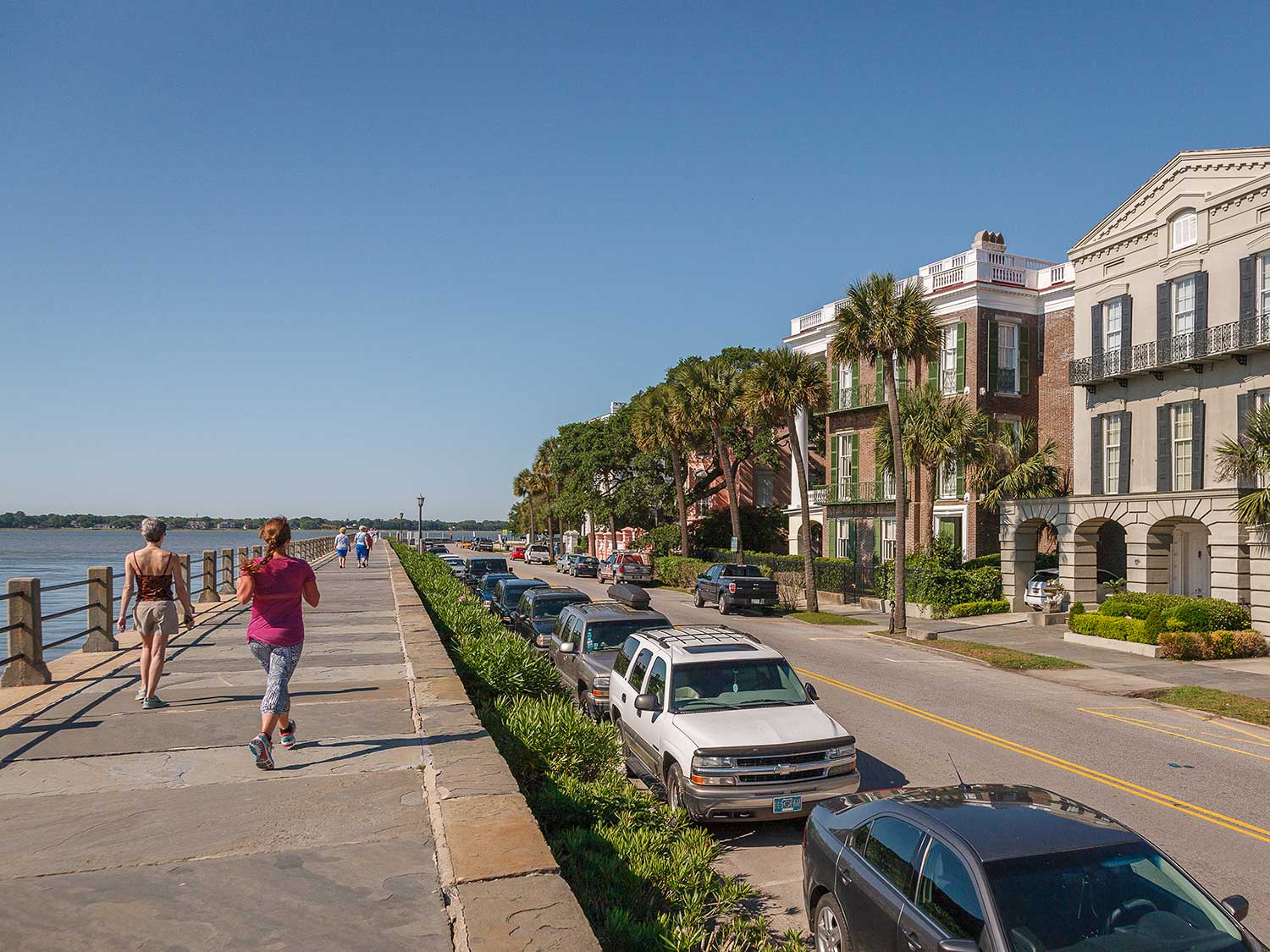 People walking on a sidewalk next to a bayside town.