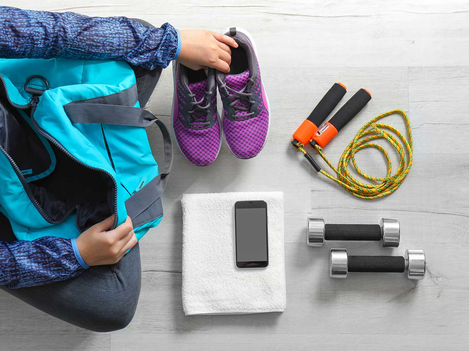 Woman packing tennis shoes, jump rope, weights, towel, and phone.