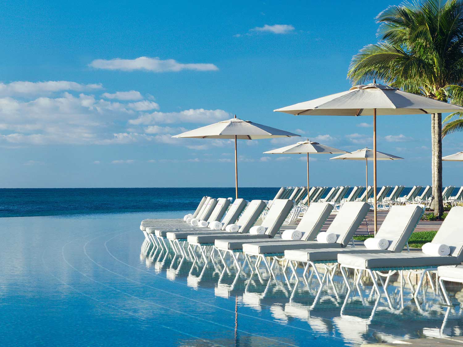 A lineup of lounge chairs next to a resort style pool.