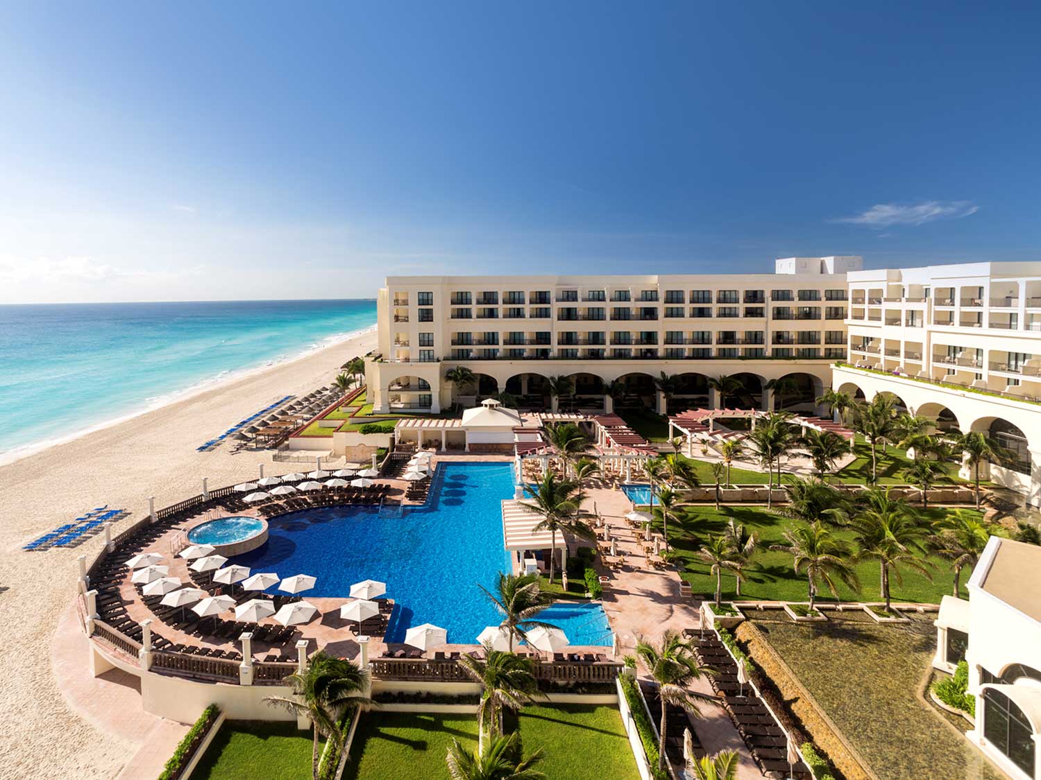 An aerial photo of of a beach resort showing the resort grounds, pool, building and ocean beside it.