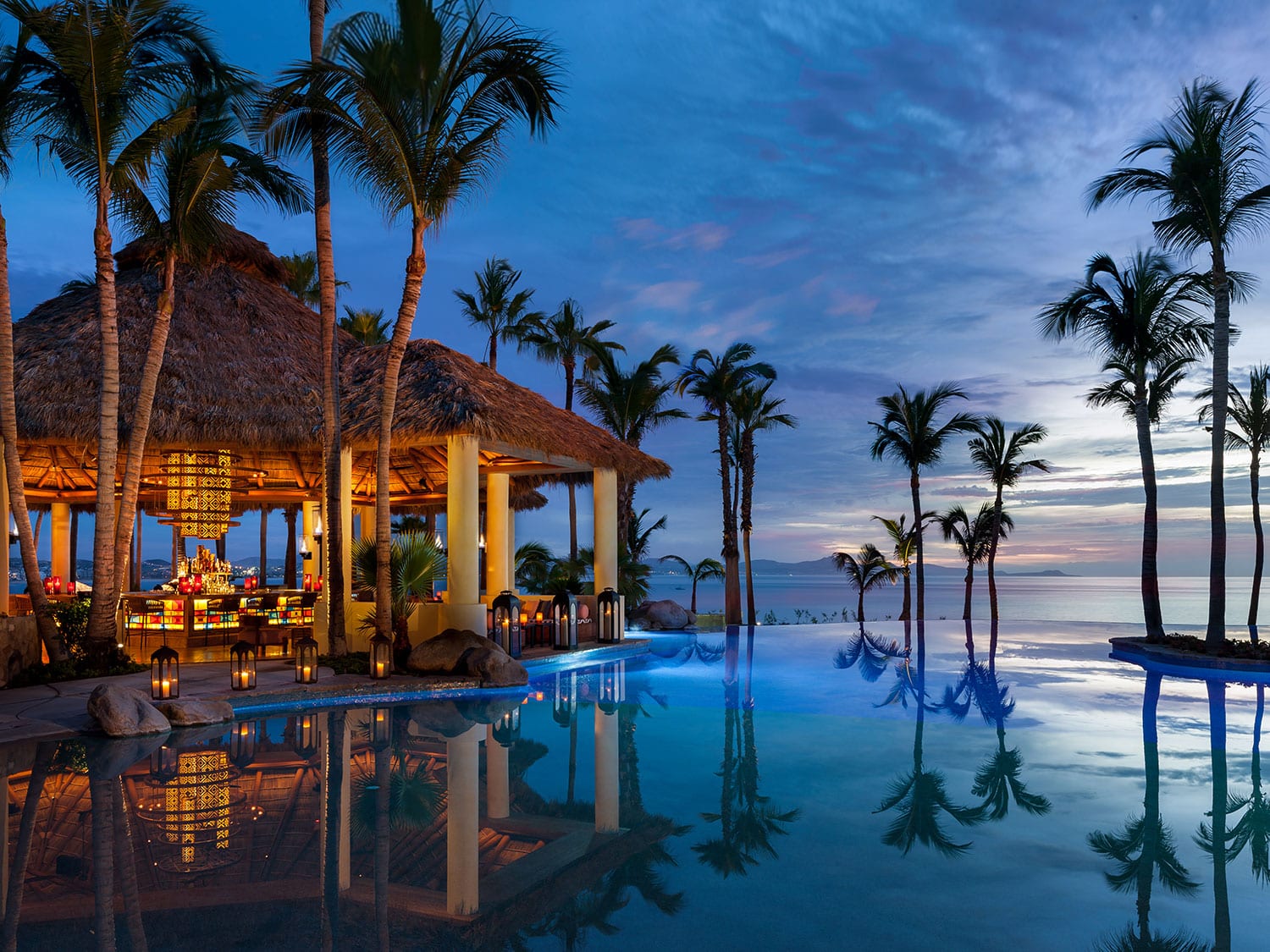 A luxury resort style pool by the ocean and a lit up pagoda.