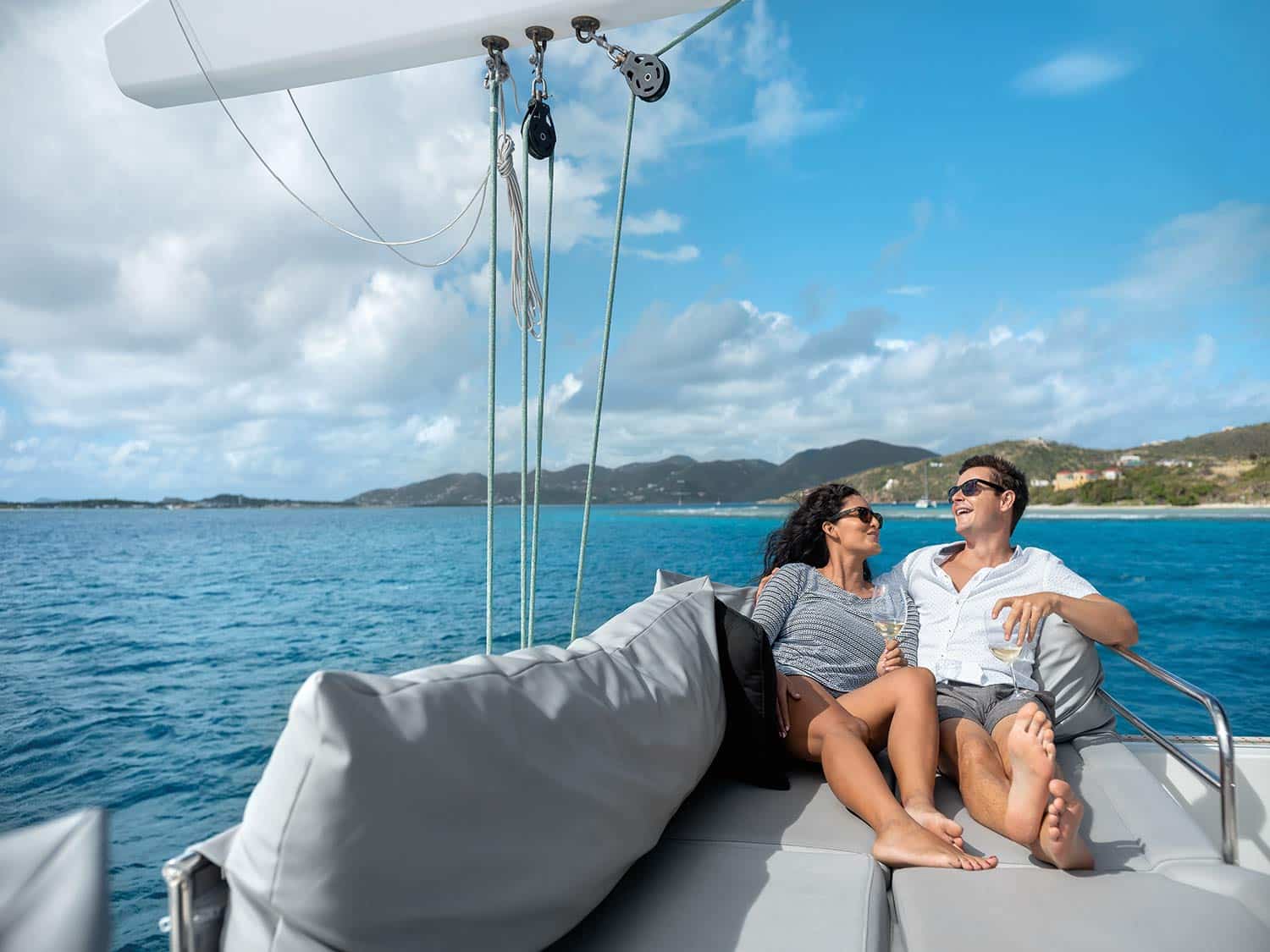 A man and woman lounge on the seats of a catamaran at sea.