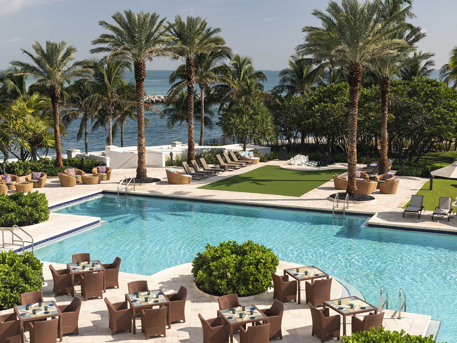 A resort style pool surrounded by palms and dining.