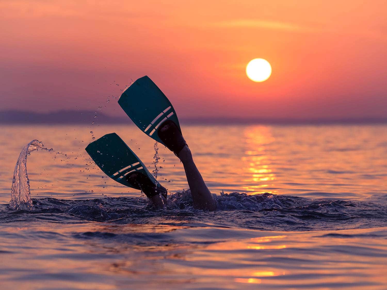 Person with snorkel fins up during sunset