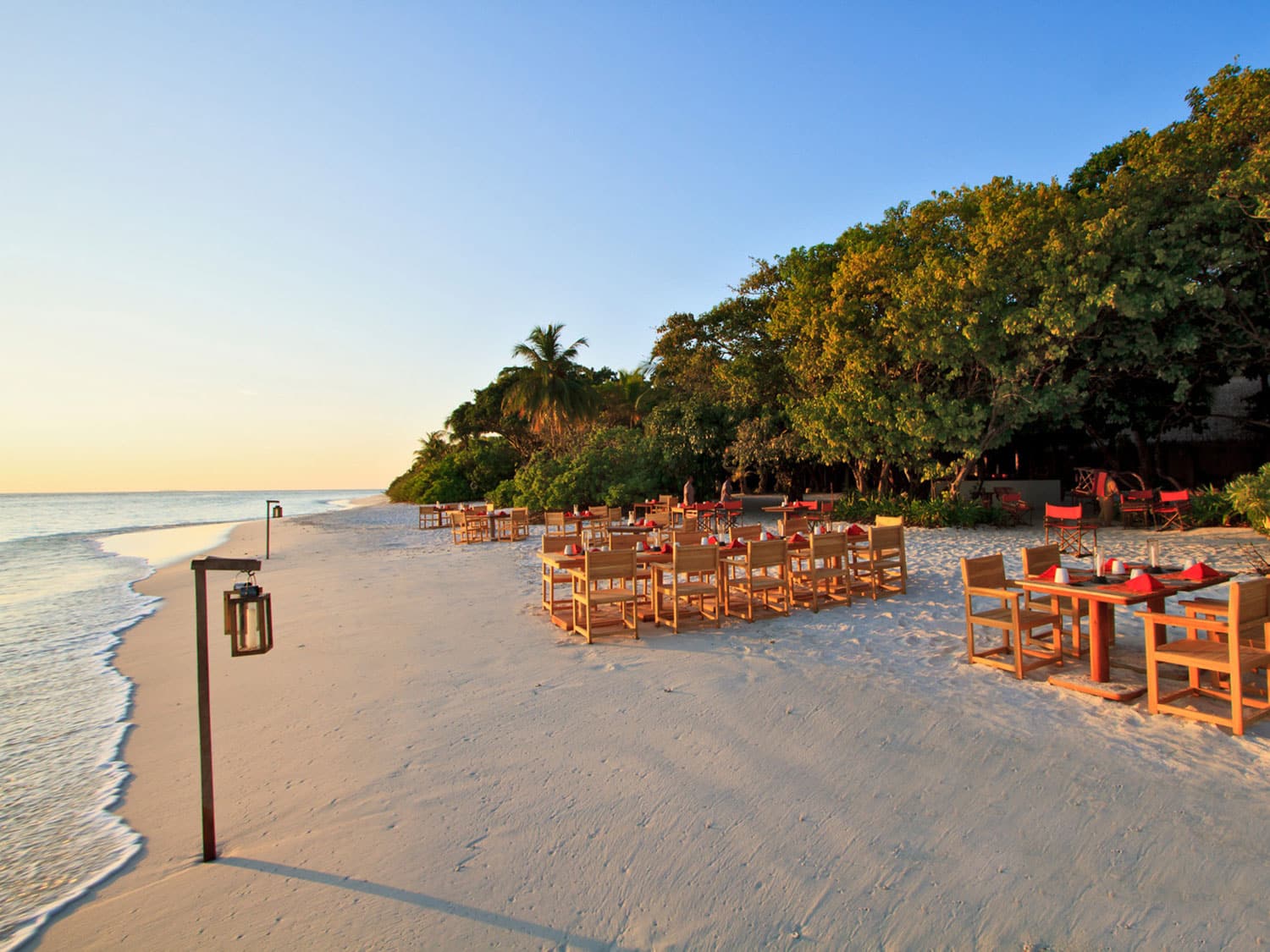 Chairs and tables arranged on an island beach at sunset.