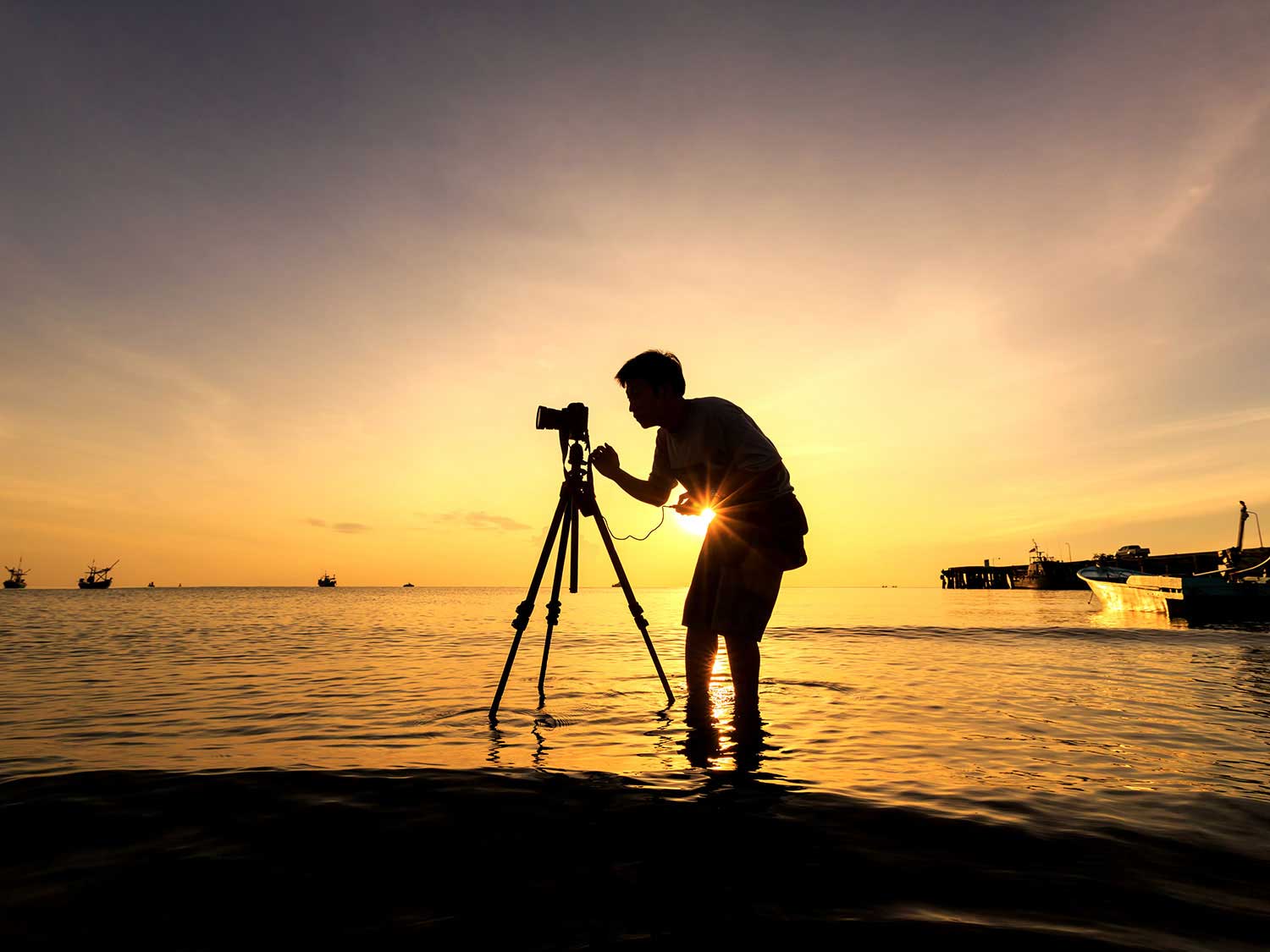Man taking photos on beach at sunset.