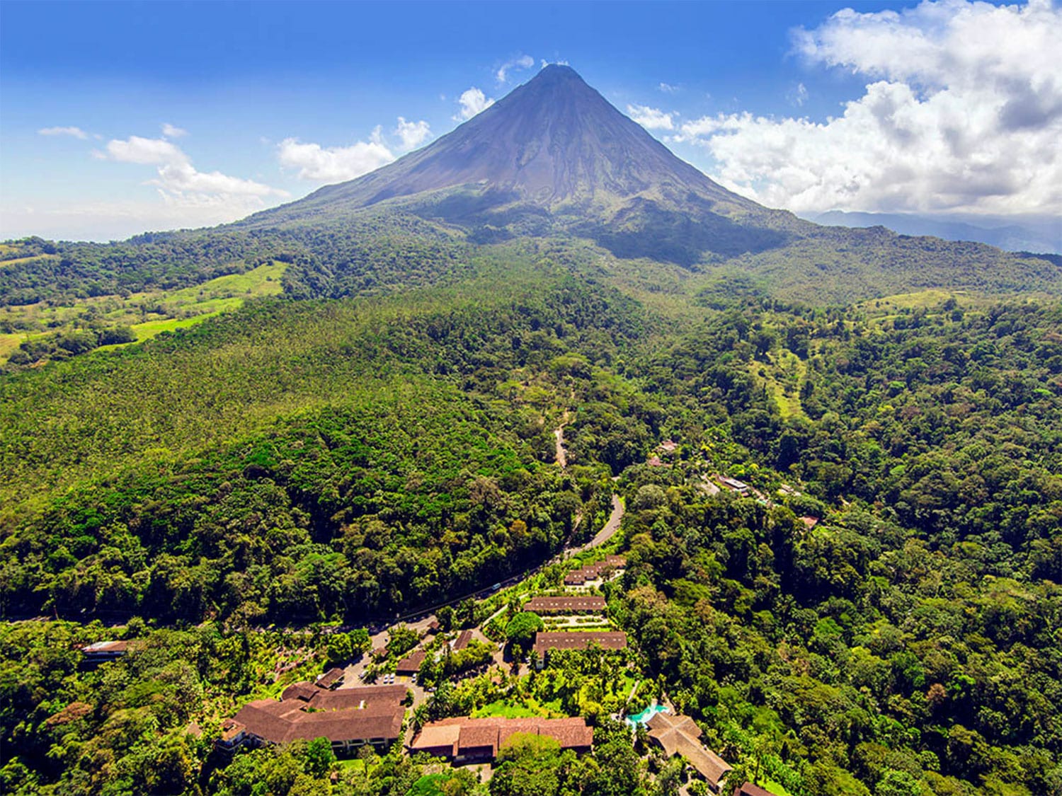 Aerial view of the Tabacón Thermal Resort and Spa surrounded by lush forests and a mountain in the distance.