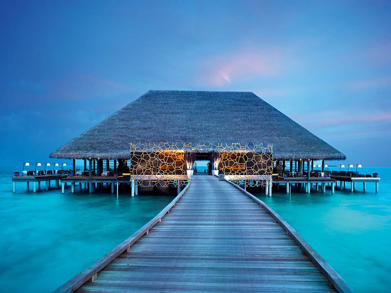 A bungalow at the end of a pier over the ocean.