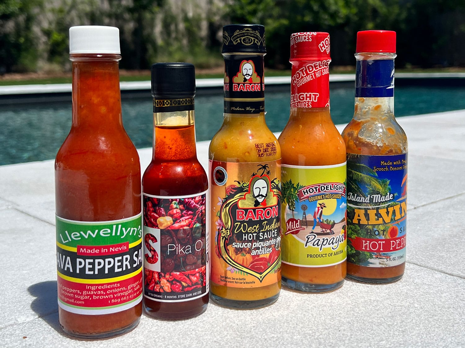Five bottles of Caribbean hot sauce, including Llewellyn’s Guava Pepper Sauce, Hot Delight Papaya, Baron West Indian Hot Sauce, Alvin’s Hot Sauce, and Spika Oil.