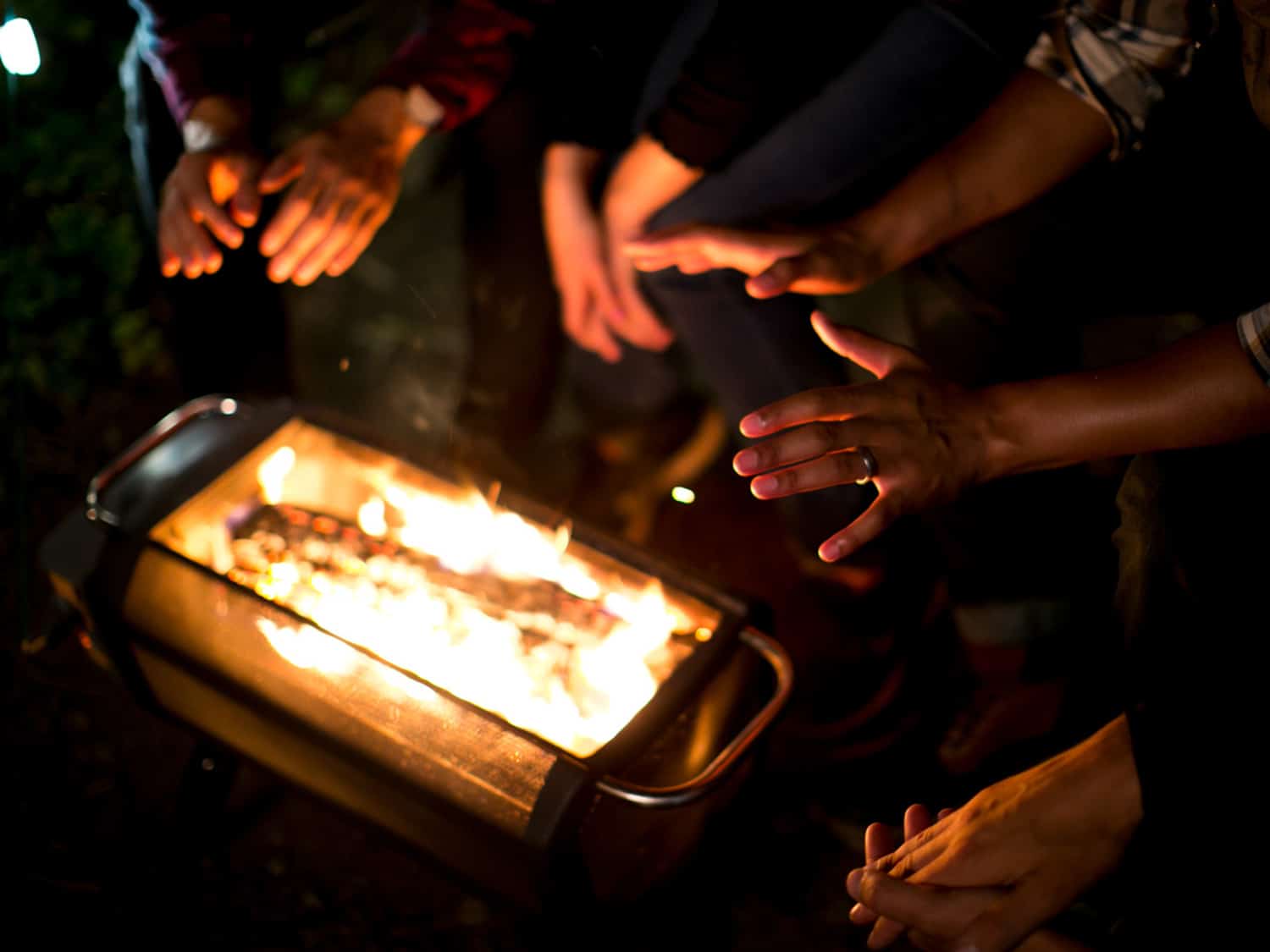 Campers gathered around the BioLite FirePit+ in the woods.