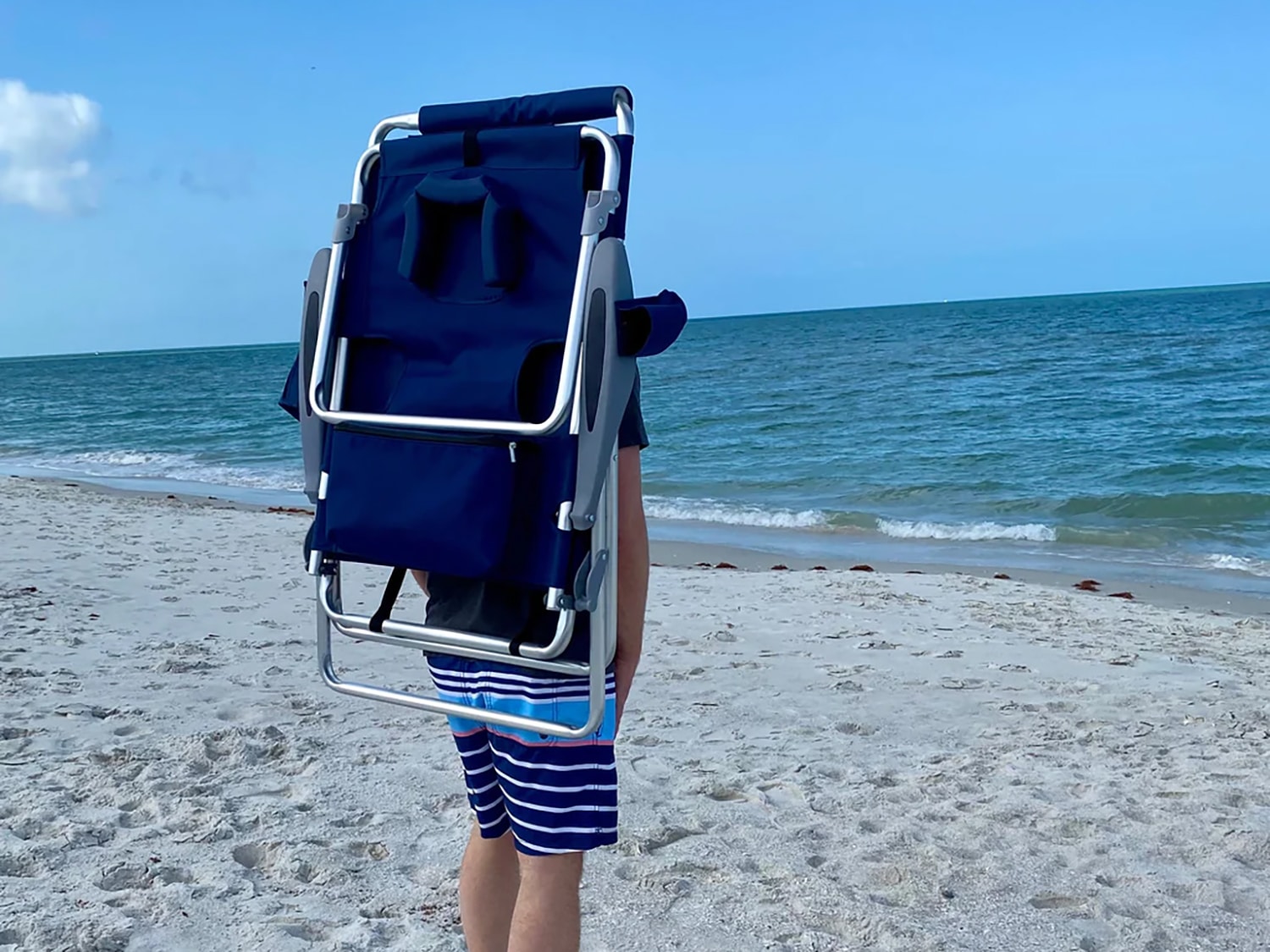 A man carrying the Ostrich 3N1 Backpack Beach Chair on a beach.