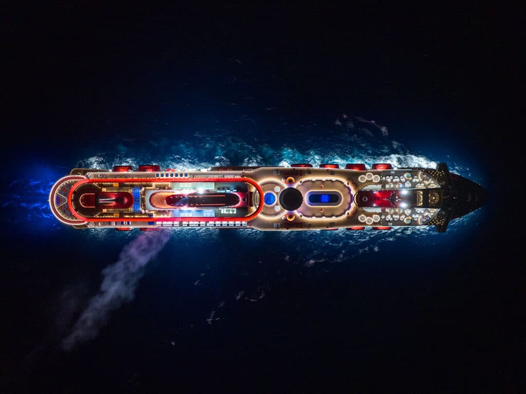 An aerial view of the Virgin Voyages Scarlet Lady cruise ship on the open waters at night.